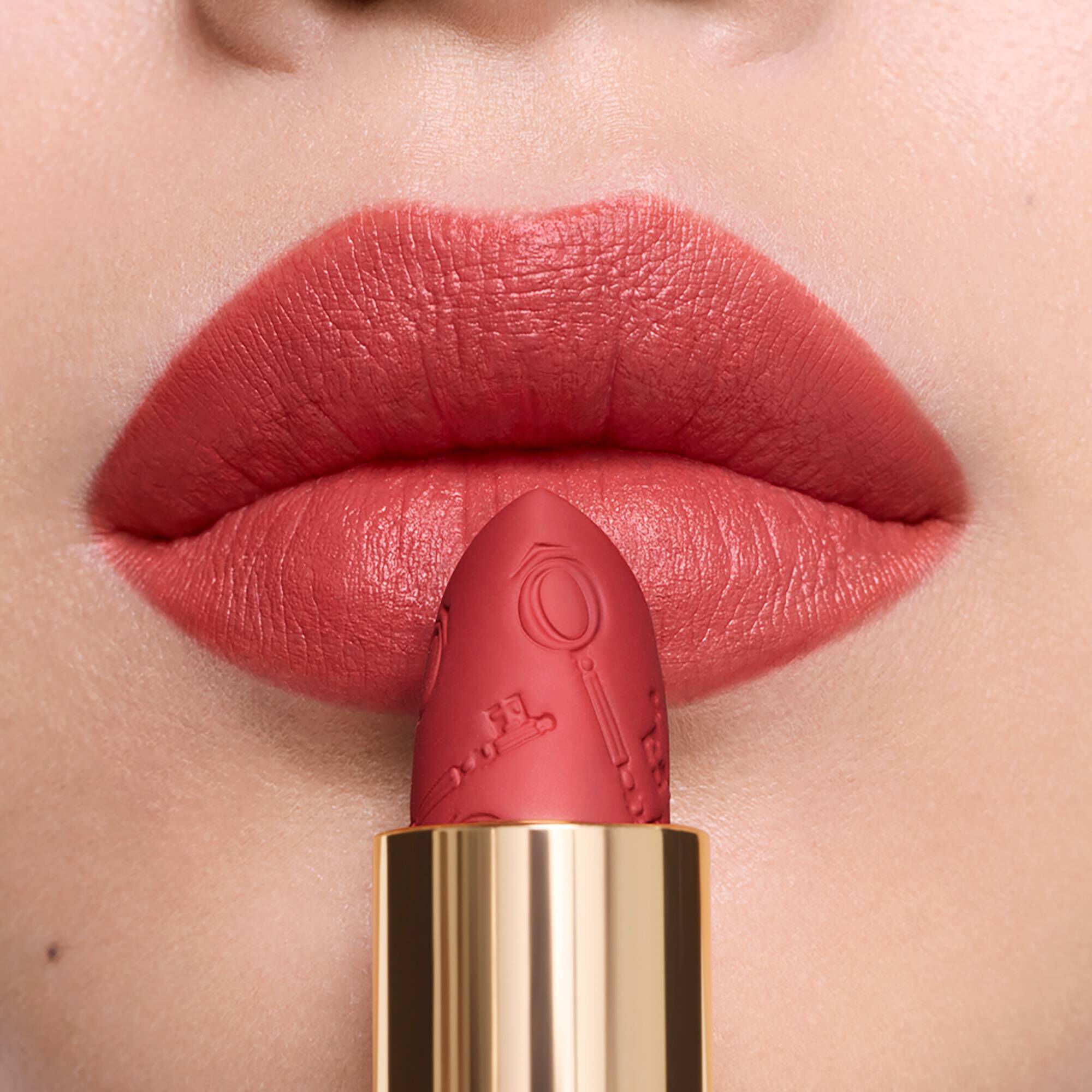 A close-up of warm matte lipstick on lips, beside its matching engraved lipstick bullet.	