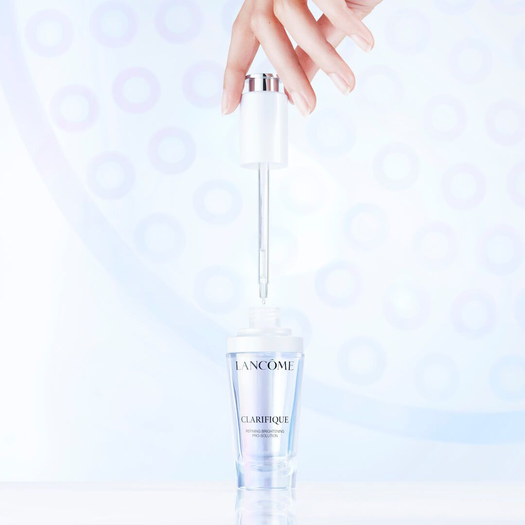 Hand holding Lancome Clarifique dropper over serum bottle emphasizing precision in serum application.
