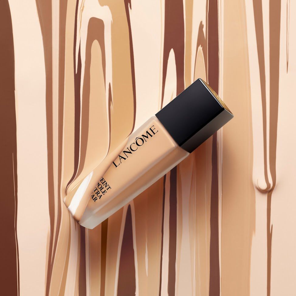 Lancome Teint Idole Ultra Wear Foundation bottle displayed on a background of flowing foundation shades, emphasizing versatile coverage and finish