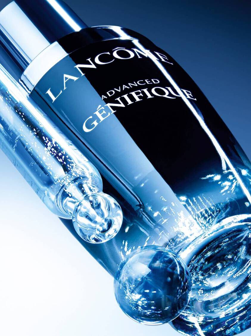 Lancome Advanced Genifique serum bottle in a futuristic blue lighting setting highlighting its sleek, modern design and advanced skincare technology.