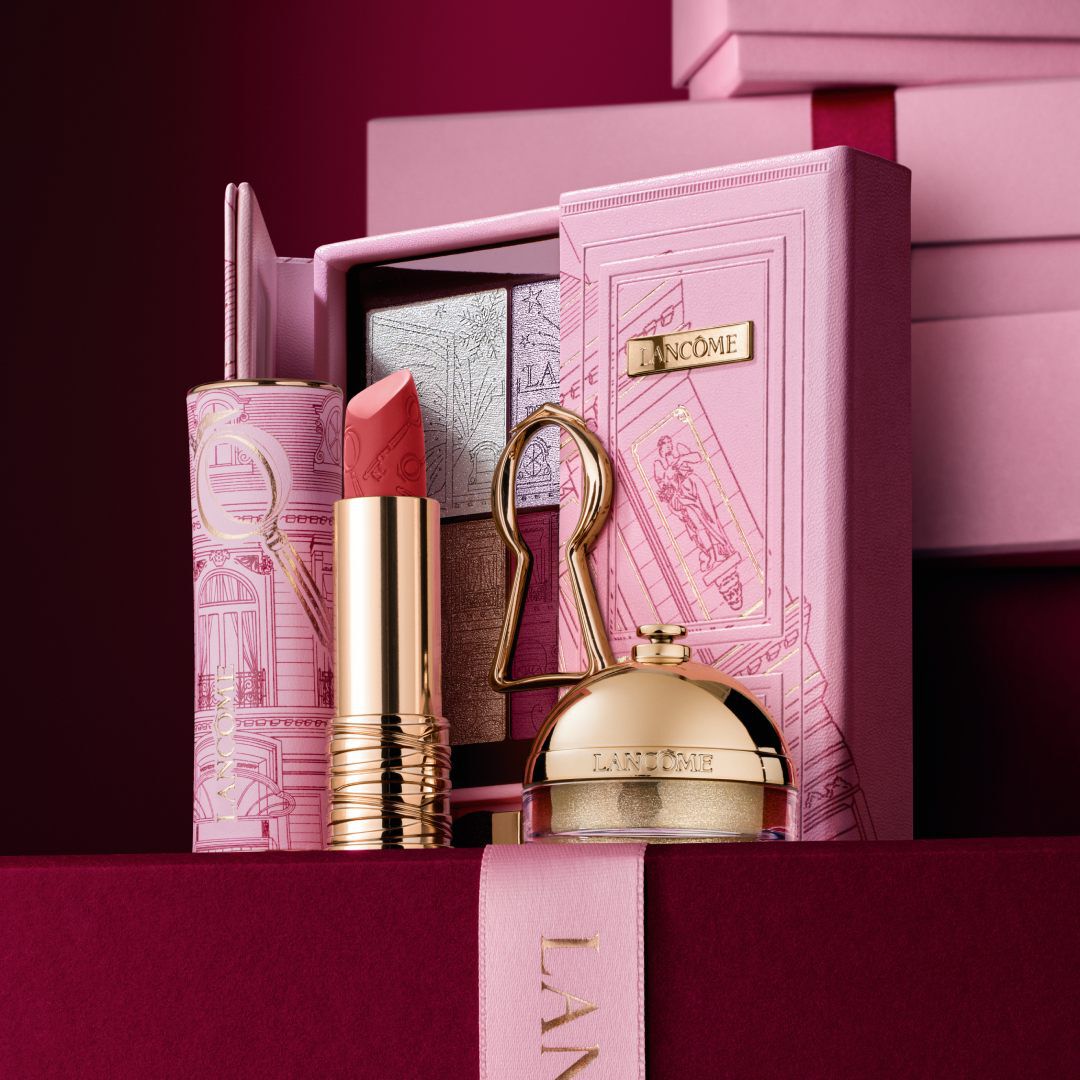 A curated Lancome holiday gift set featuring a lipstick, eyeshadow palette, and gold beauty products displayed against a decorative pink case.